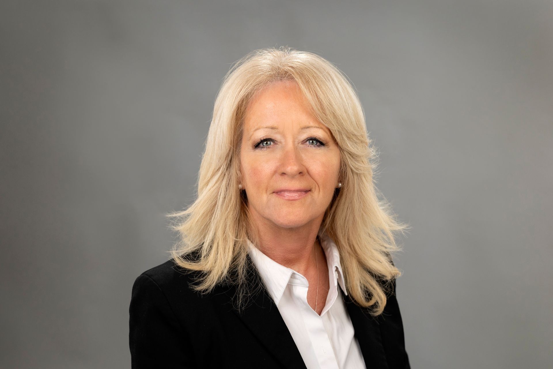 Portrait of a woman with blonde hair wearing a black blazer and white shirt against a gray background.
