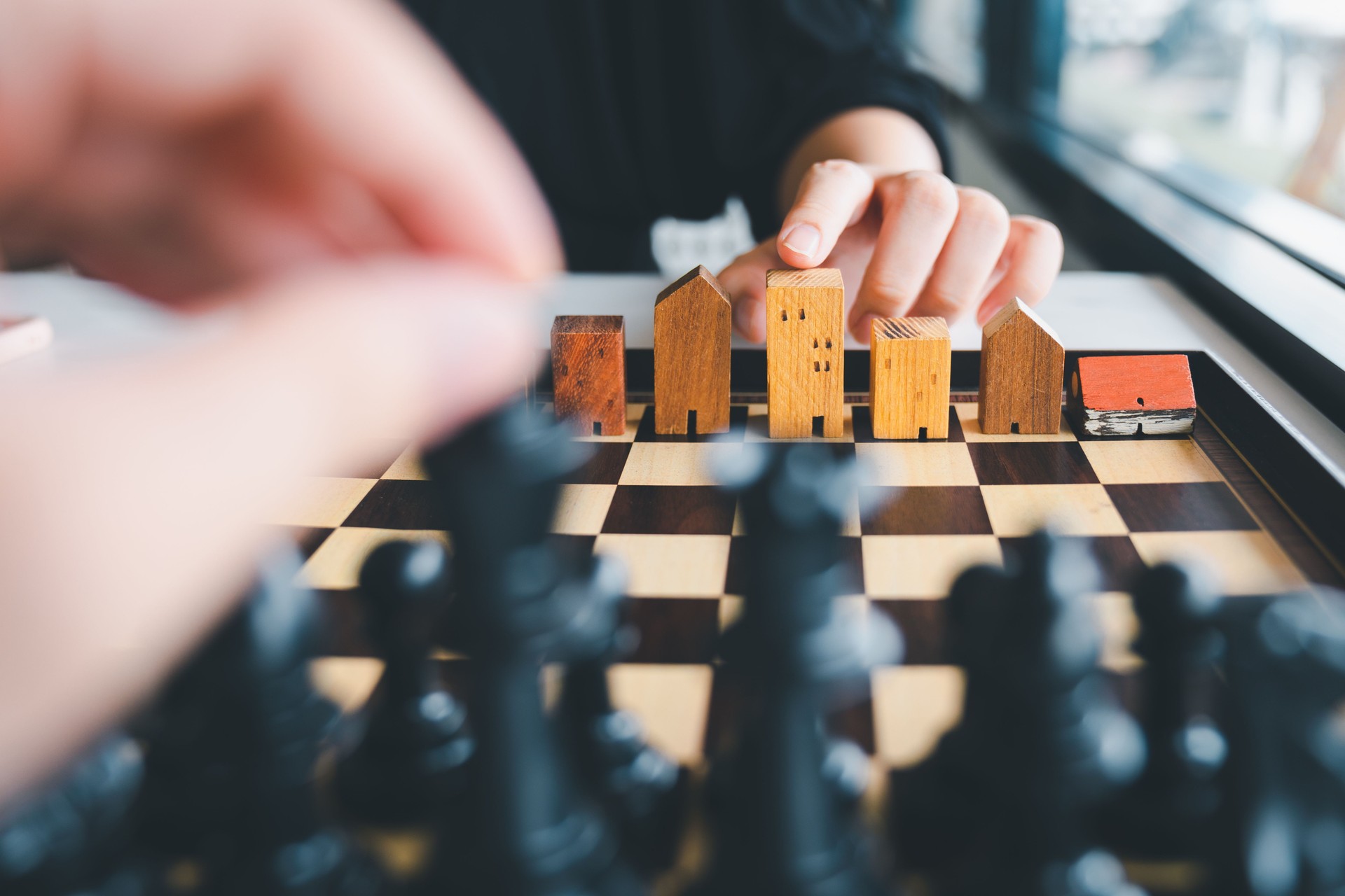 Hand of business man moving chess to Building and house models in chess game, competition success play. strategy, management or leadership concept